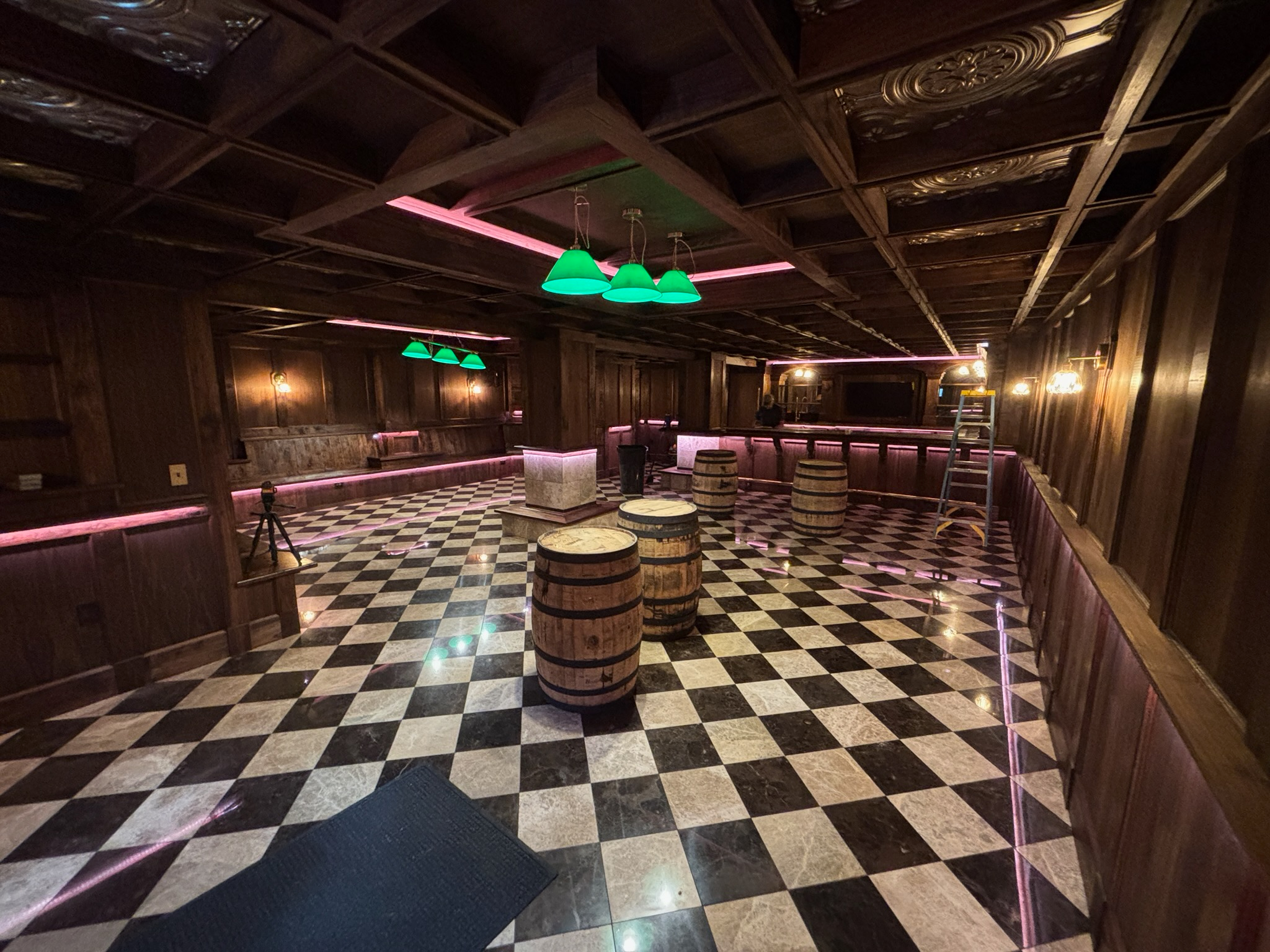 Custom residential speakeasy with dark wood paneling, checkerboard floor, bar, and green pendant lights